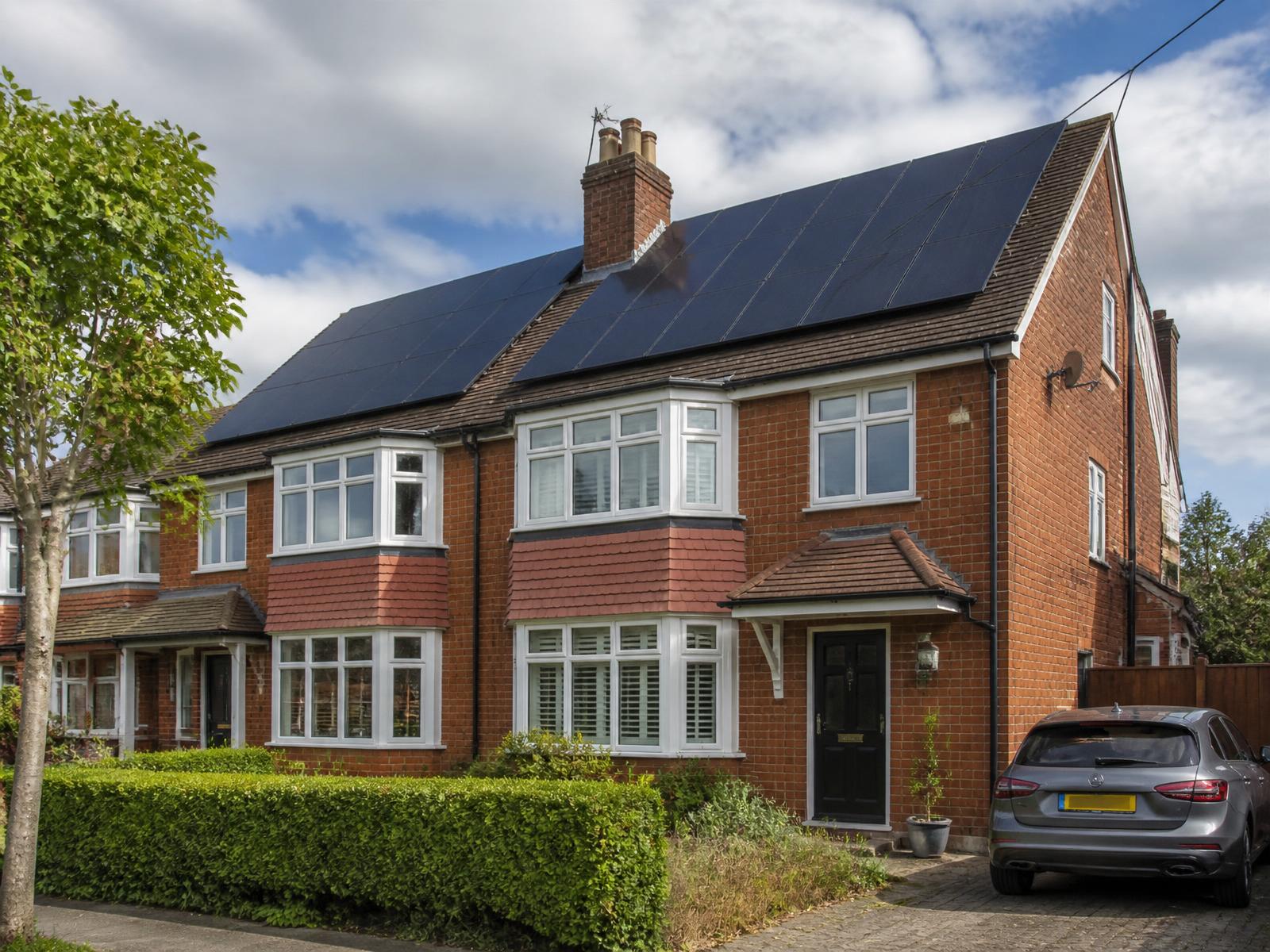 A red-brick UK semi-detached home with black solar panels fitted across its pitched roof